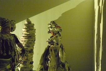 4 Personen in Kostümen aus Zeitungspapier. An die Wand werden ihre Schatten geworfen.